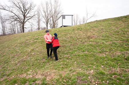 Two friends are playfully engaging in a fun activity on a gently sloping green hill during early spring. The atmosphere is lighthearted and cheerful.の写真素材