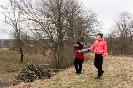 Two individuals walk through a tranquil area, carrying yoga mats in preparation for a relaxing outdoor session amidst nature's beauty on a cool, overcast day.の写真素材