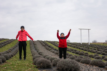 Two individuals engage in a joyful exercise session amidst rows of lavender, celebrating family connections and the beauty of nature on a cool, overcast day.の写真素材