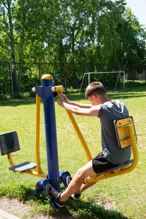 A young person uses a leg press machine at an outdoor gym. The scene is bright and sunny, showcasing...