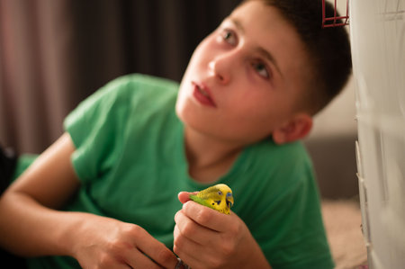 A young boy lies down, carefully holding a small, yellow budgie. The scene is intimate and peaceful, showing a tender moment between a child and their pet.の写真素材