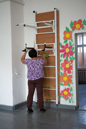 A woman cleans a wall-mounted ladder with a green cloth. The ladder stands next to a wall painted...