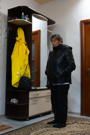 This interior shot shows a woman near a coat rack holding a yellow jacket, complemented by a mirror, drawers and storage shelves. The setting is intimate, possibly within a home's entryway.の写真素材