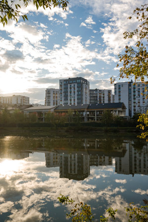 As the sun sets, the water mirrors the contemporary buildings, creating a tranquil scene where nature meets urban life amidst the gentle autumn breeze.の写真素材