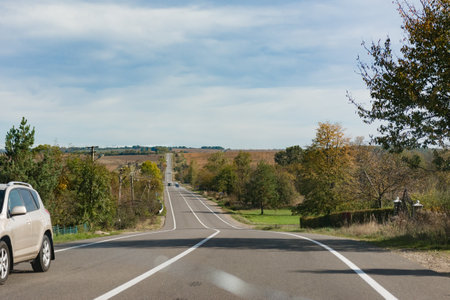 A peaceful country drive unfolds with gentle curves and expansive fields under a clear sky. Warm autumn hues paint the landscape, inviting exploration and adventure.の写真素材