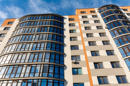 Tall building showcases contemporary architectural elements with its curved glass windows and vibrant colors set against a sunny day, creating an inviting urban atmosphere.の写真素材