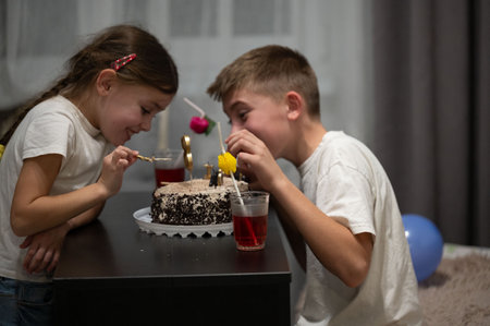 Two children delight in a birthday celebration, sharing cake at a table adorned with colorful...
