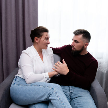 Two individuals express deep emotions while sitting closely on a soft chair, sharing an intimate dialogue that reflects trust and vulnerability.の写真素材