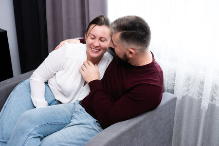 Share a warm and intimate moment as a couple snuggles together on a comfortable couch, basking in joy and connection during a relaxed day indoors.の写真素材