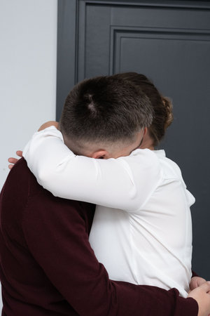 Two individuals share a heartfelt hug in a modern and minimalistic indoor space, conveying love and support in a quiet moment together.の写真素材