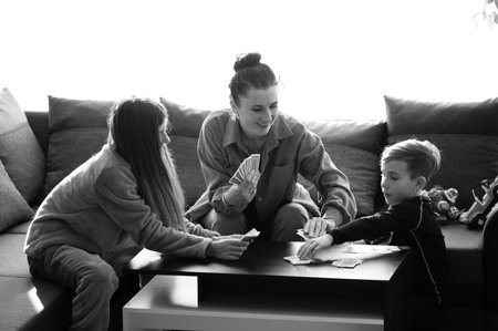 Two children and a parent engage in a fun card game at a stylish table, surrounded by a warm,...