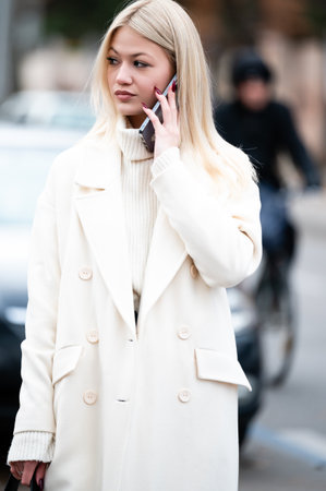 Amidst a bustling urban backdrop, a stylish figure in a white coat converses on the phone, embodying...