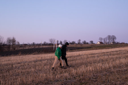In a peaceful rural setting, two friends take a leisurely walk through a recently harvested field, savoring the calm of an early spring evening under a fading sky.の写真素材