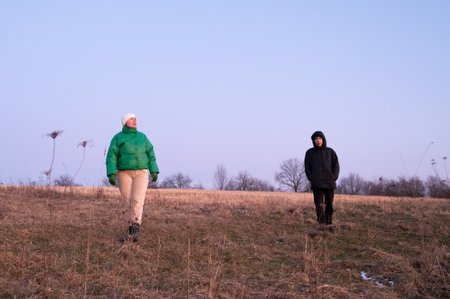 Two friends wander through a serene open field during twilight, dressed warmly for the cool evening air, enjoying the peaceful atmosphere of nature.の写真素材