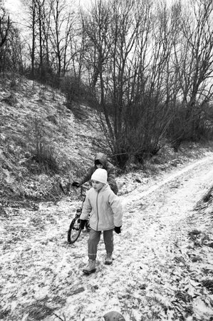 Children trek through a snowy path, bundled in warm coats and hats, as trees loom closely around. Their laughter fills the crisp winter air, creating a magical atmosphere.の写真素材