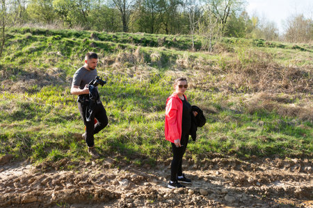 Two friends venture along a muddy trail, one capturing the beauty of nature with a camera while the other strolls casually in vibrant spring attire.の写真素材