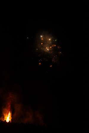 Brightly colored fireworks burst into the starry sky while a bonfire crackles below, creating a captivating atmosphere filled with excitement and joy during a local festivity.の写真素材
