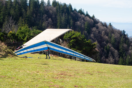 Gliders prepared for flight rest on a green hillside as enthusiasts gather nearby, enjoying the thrill of tandem hang gliding against the crisp mountain backdrop.の写真素材