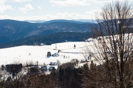 Rolling hills glisten in snow, dotted with charming villages. The bright sky contrasts with the serene winter scene, inviting a sense of calm and beauty in nature.の写真素材