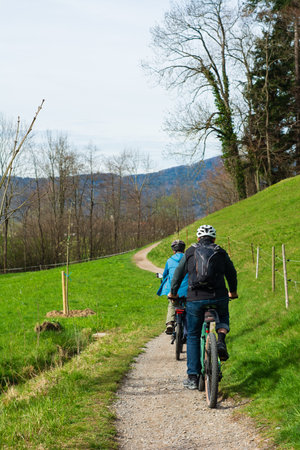 Two cyclists navigate a picturesque trail surrounded by lush greenery and gentle hills, enjoying the tranquility of nature during a spring day.の写真素材