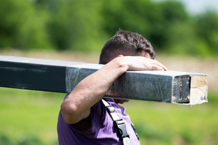 A man carries a wooden beam for installing a gazebo in a lavender field, installation work.の写真素材