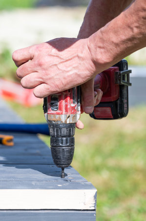 Installation work of a wooden gazebo, the master screws the screws close-up into the wooden floor.の写真素材