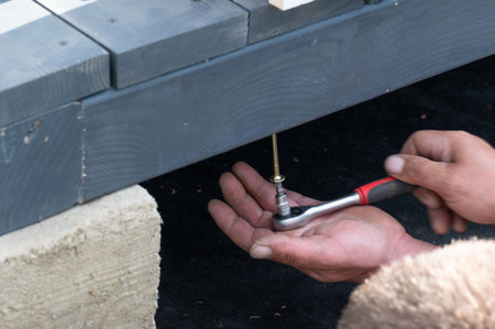 A man manually tightens a screw into the gazebo support to secure the floor to the frame, the work is related to installation.の写真素材