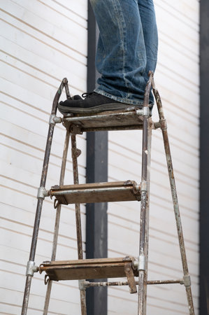 Male legs standing on a metal ladder with wooden steps, a worker and work equipment.