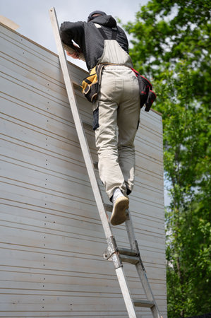 A worker climbs up a ladder during the construction of a gazebo, construction work.の写真素材