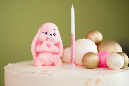 A close-up shot of a delicious-looking cake decorated with a cute bunny figurine and pastel-colored spheres. A single candle stands beside the bunny.の写真素材