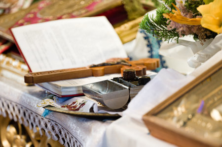 Close-up of religious articles on a table, including an open book, a wooden cross, and a small metal vessel. The setting appears to be a church or religious site.の写真素材