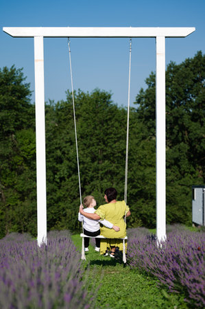 A heartwarming scene of a woman and young child sharing a peaceful moment on a swing set, surrounded by vibrant purple lavender blossoms. The sunny day enhances the tranquility.の写真素材