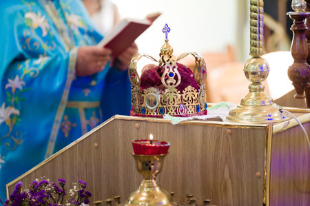 A golden crown rests on a wooden altar, next to a lit candle. A person in blue robes is visible in the background, suggesting a religious ceremony.の写真素材