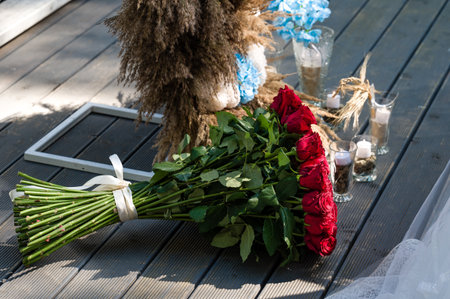 A vibrant bouquet of red roses lies on a dark gray wooden deck. Nearby are decorative items including candles and dried flowers, suggesting a romantic or celebratory setting.の写真素材