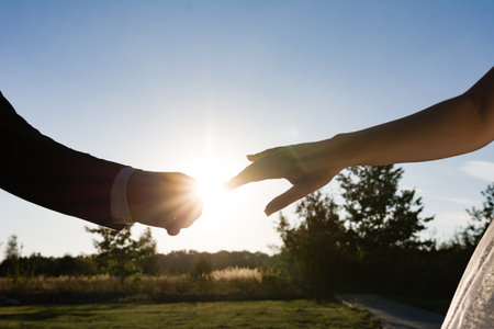 Silhouetted hands reach for one another against a vibrant sunset. The image evokes feelings of love, connection, and hope. A serene outdoor setting completes the scene.の写真素材