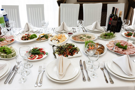 A beautifully arranged banquet table showcases a variety of cold cuts, salads, and appetizers. Elegant place settings and wine bottles complete the scene, suggesting a formal celebration or reception.の写真素材