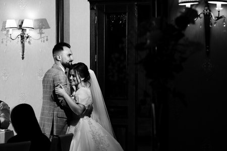 A black and white photograph of a bride and groom sharing a tender moment at their wedding reception. The couple is elegantly dressed, and the setting is refined.の写真素材