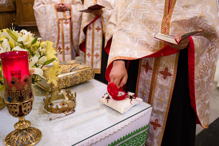 A priest in ornate robes prepares wedding rings on a pillow during a religious ceremony. Candles, flowers, and a crown are visible on the altar.の写真素材
