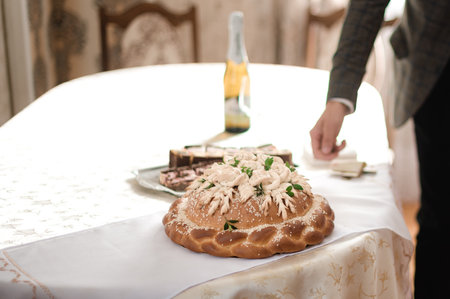 A beautifully decorated loaf of bread, possibly a ceremonial one, sits on a table alongside other pastries and a bottle. The setting appears formal, perhaps a wedding or other special event.の写真素材
