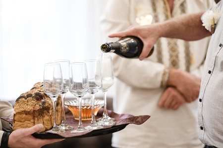 A person pours sparkling wine into several champagne flutes arranged on a serving tray with a loaf of bread and a small bowl of honey.の写真素材