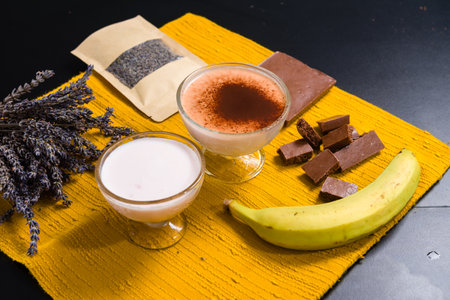 Two dessert cups, chocolate, banana, and lavender on a yellow mat.の写真素材