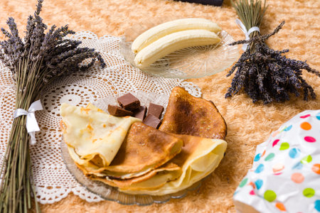 Crepes, bananas, and chocolate pieces arranged on a table with lavender bouquets.