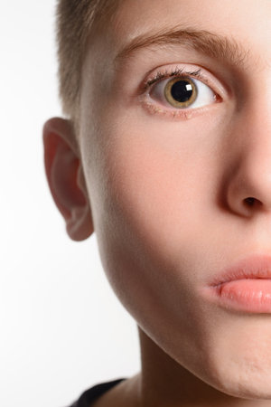 A detailed close-up shot focusing on the eye and facial features of a young person. The image highlights the texture of skin and the subtle expression. Neutral background.の写真素材