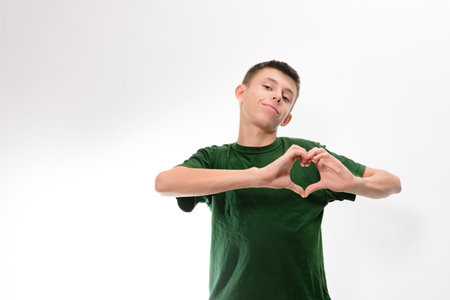 A young man in a green shirt makes a heart shape with his hands against a white background. He looks directly at the camera with a pleasant expression.の写真素材