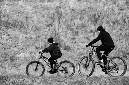 Two figures on mountain bikes cycle along a grassy path, their silhouettes contrasting against a...