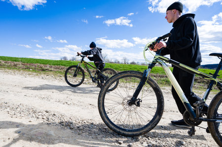 A scenic outdoor shot of two people on mountain bikes. One cycles along a gravel path, under a clear...