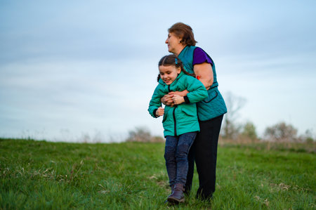 A heartwarming scene of an elderly woman embracing her granddaughter. They stand in a lush green...
