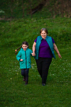 A heartwarming scene of a grandmother and her granddaughter strolling through a grassy field. The child's joyful expression is heartwarming. A beautiful moment captured.の写真素材