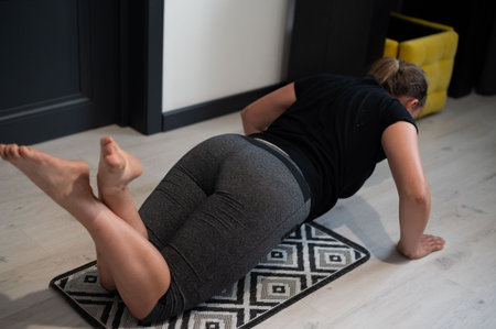 A woman in gray athletic wear performs a leg stretch on a geometric mat at home. The focus is on her lower body during the exercise.の写真素材