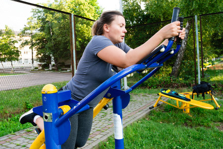 A woman uses outdoor gym equipment, focusing on a core strengthening exercise. She's in a park setting, enjoying the sunshine and fresh air.の写真素材